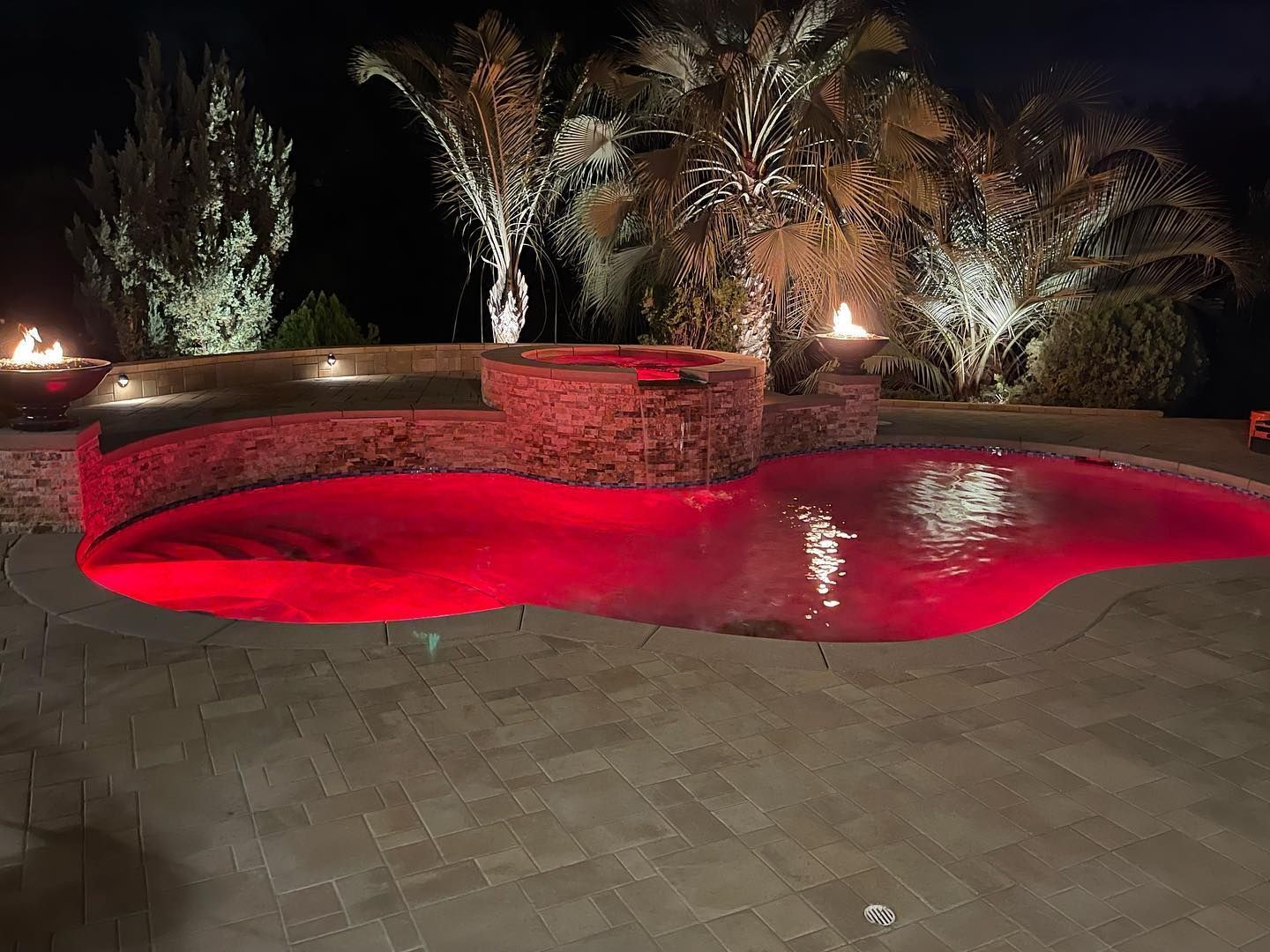 A large swimming pool is lit up with red lights at night.