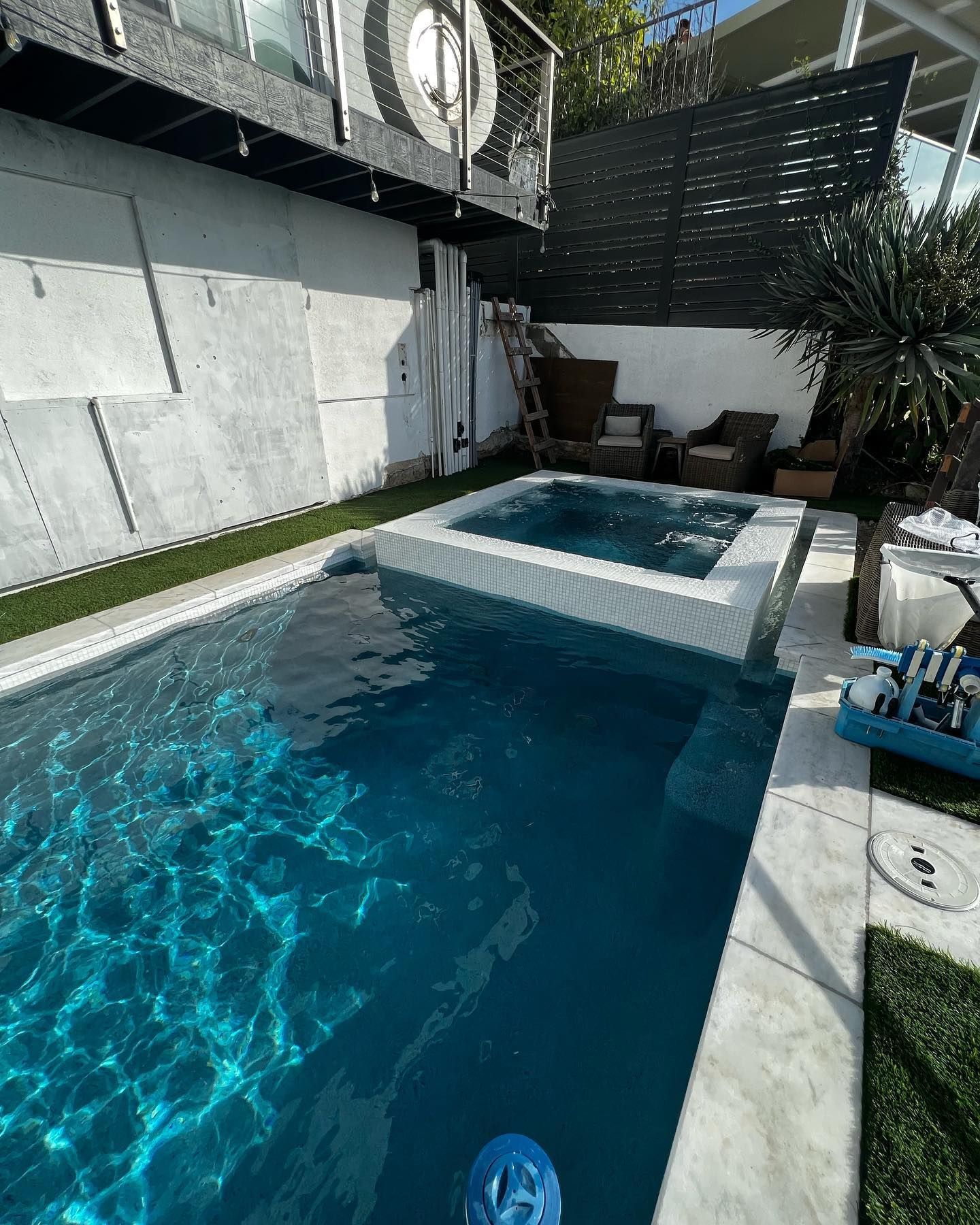 A large swimming pool with a hot tub in the backyard of a house.