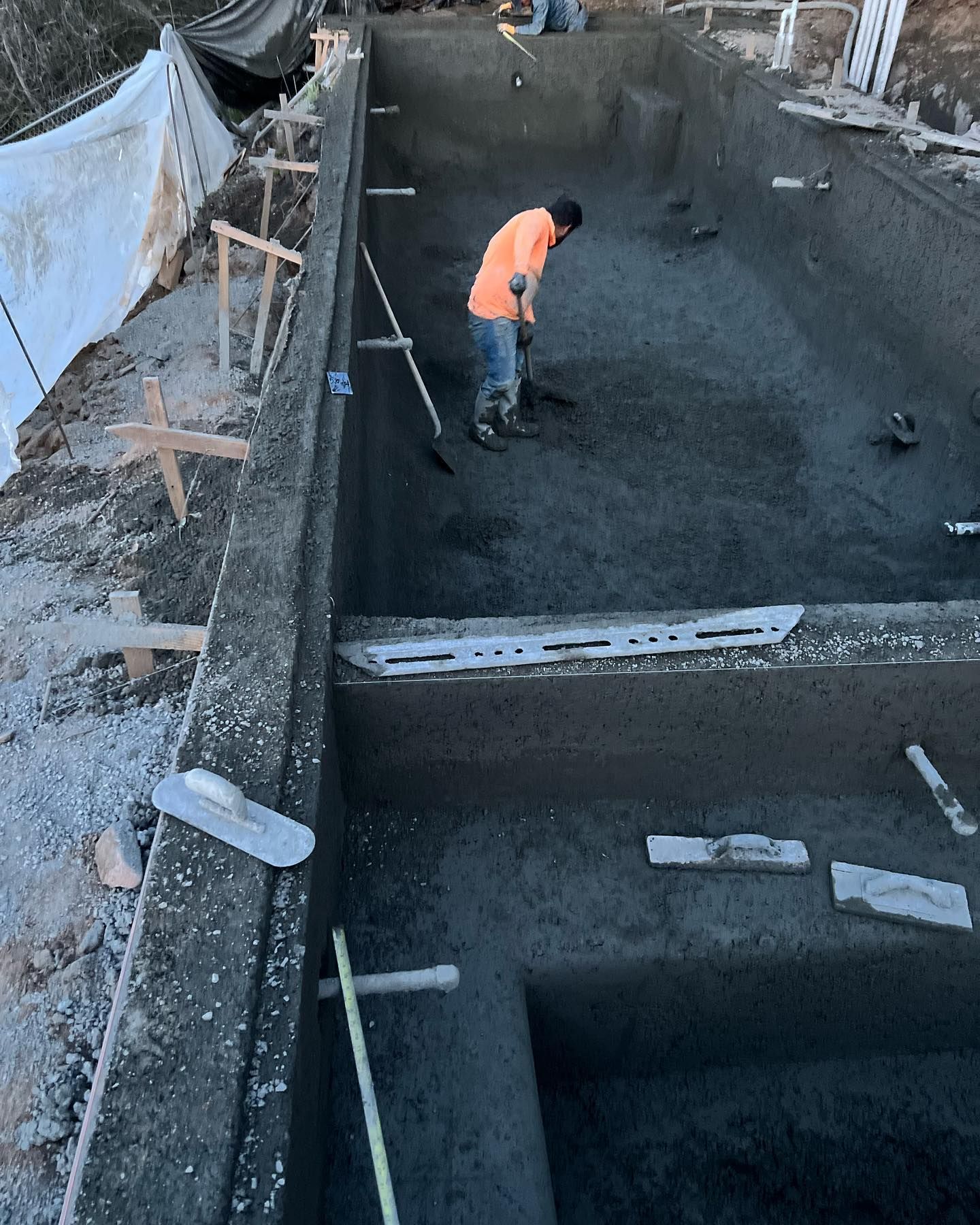 A man in an orange shirt is working on a concrete pool