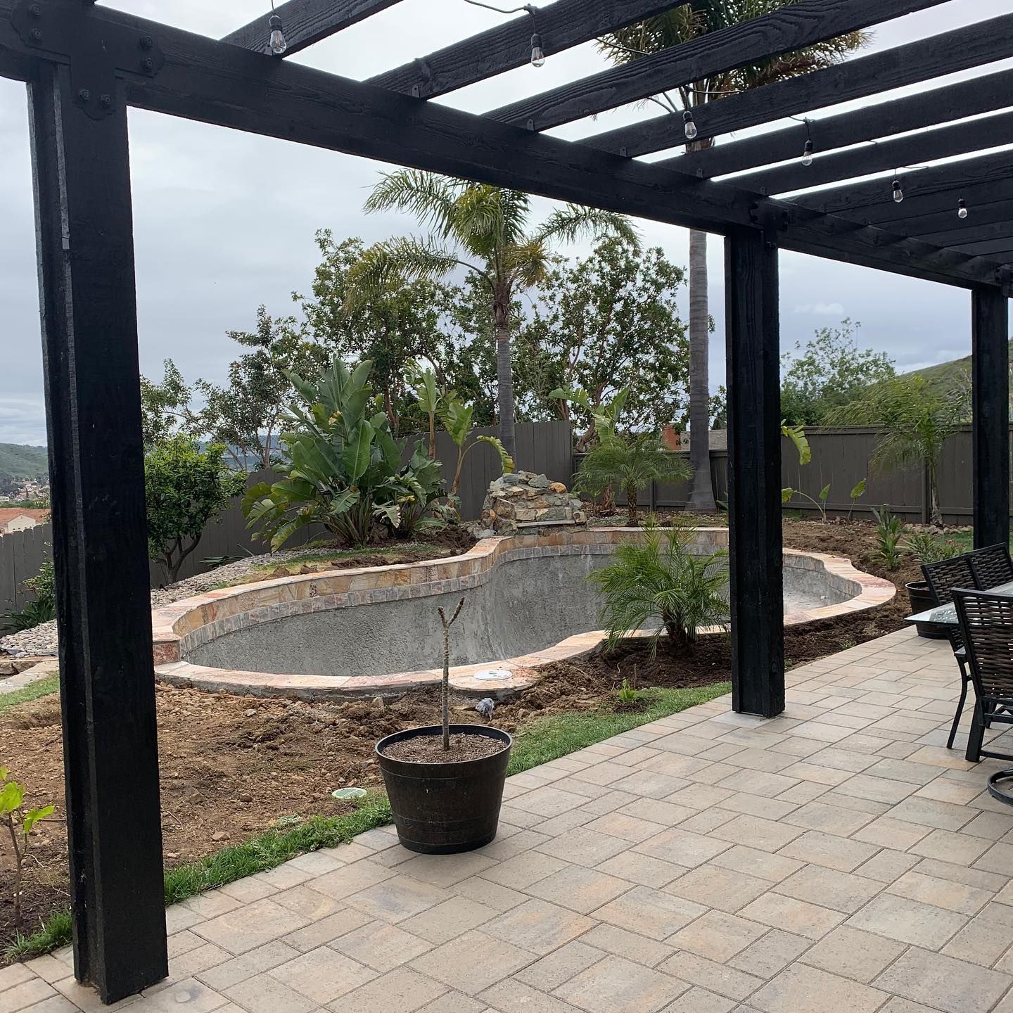 A patio with a pergola and a swimming pool in the background.