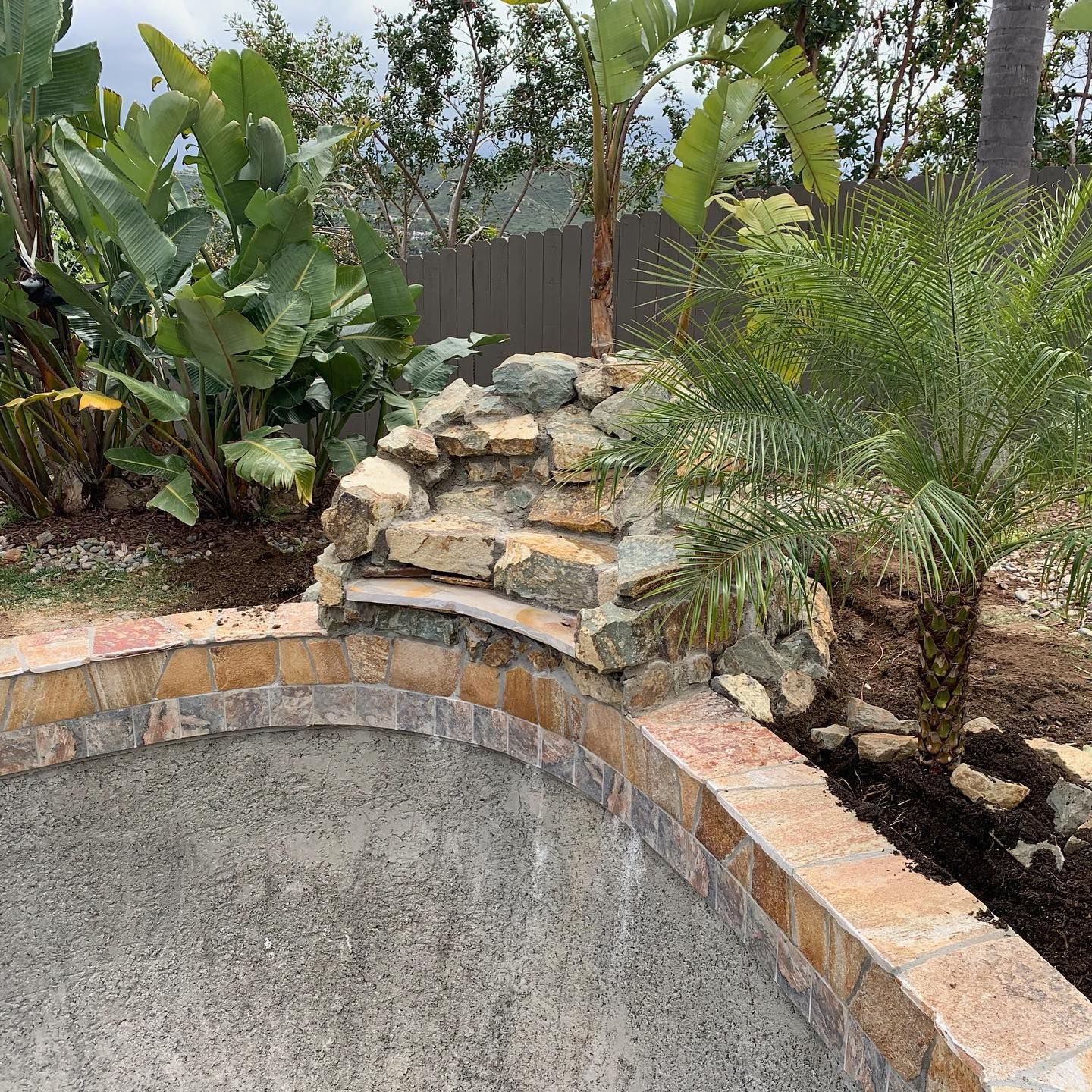 There is a waterfall in the middle of the pool surrounded by plants.