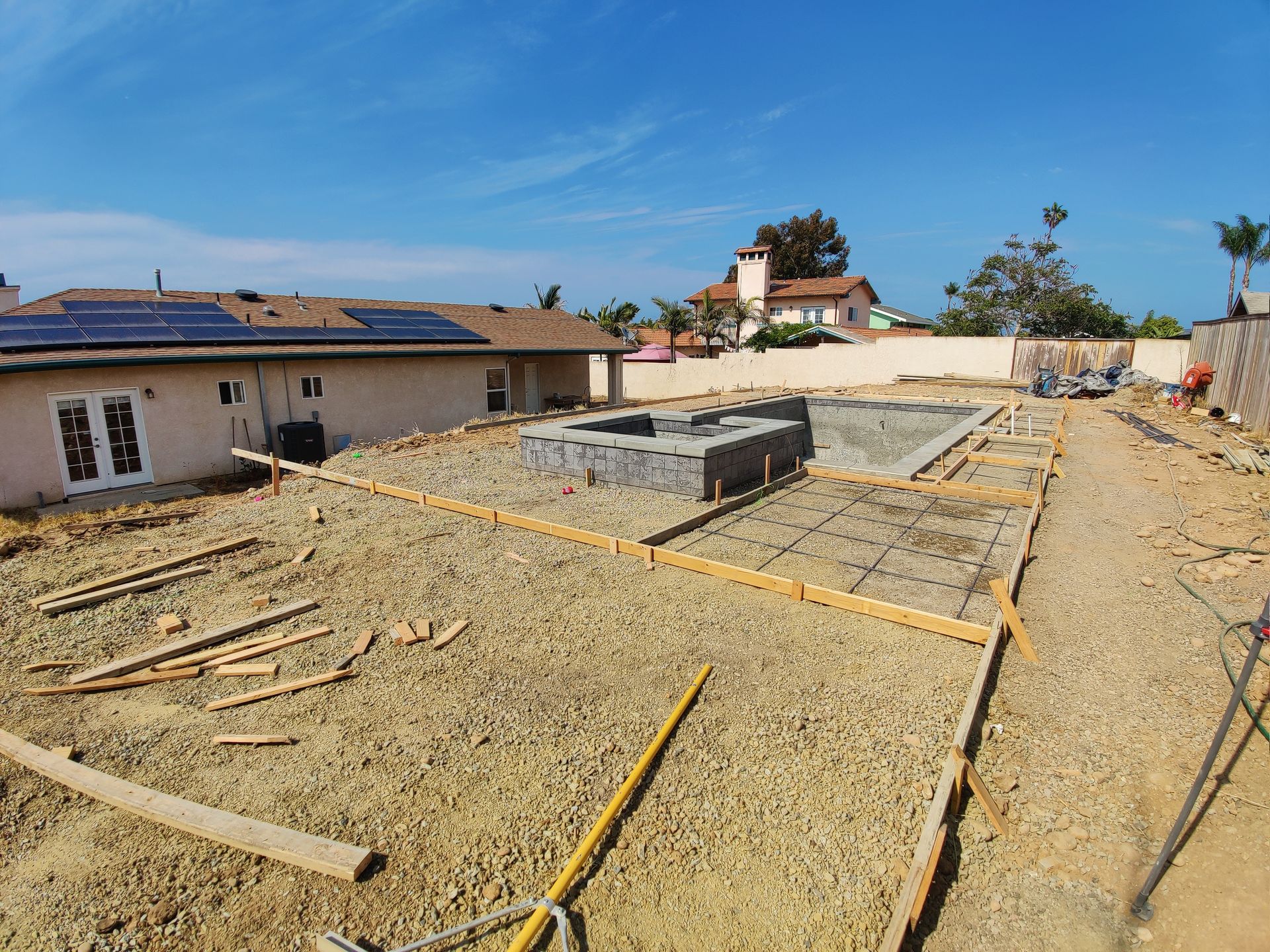 A construction site with a house in the background and a swimming pool under construction.