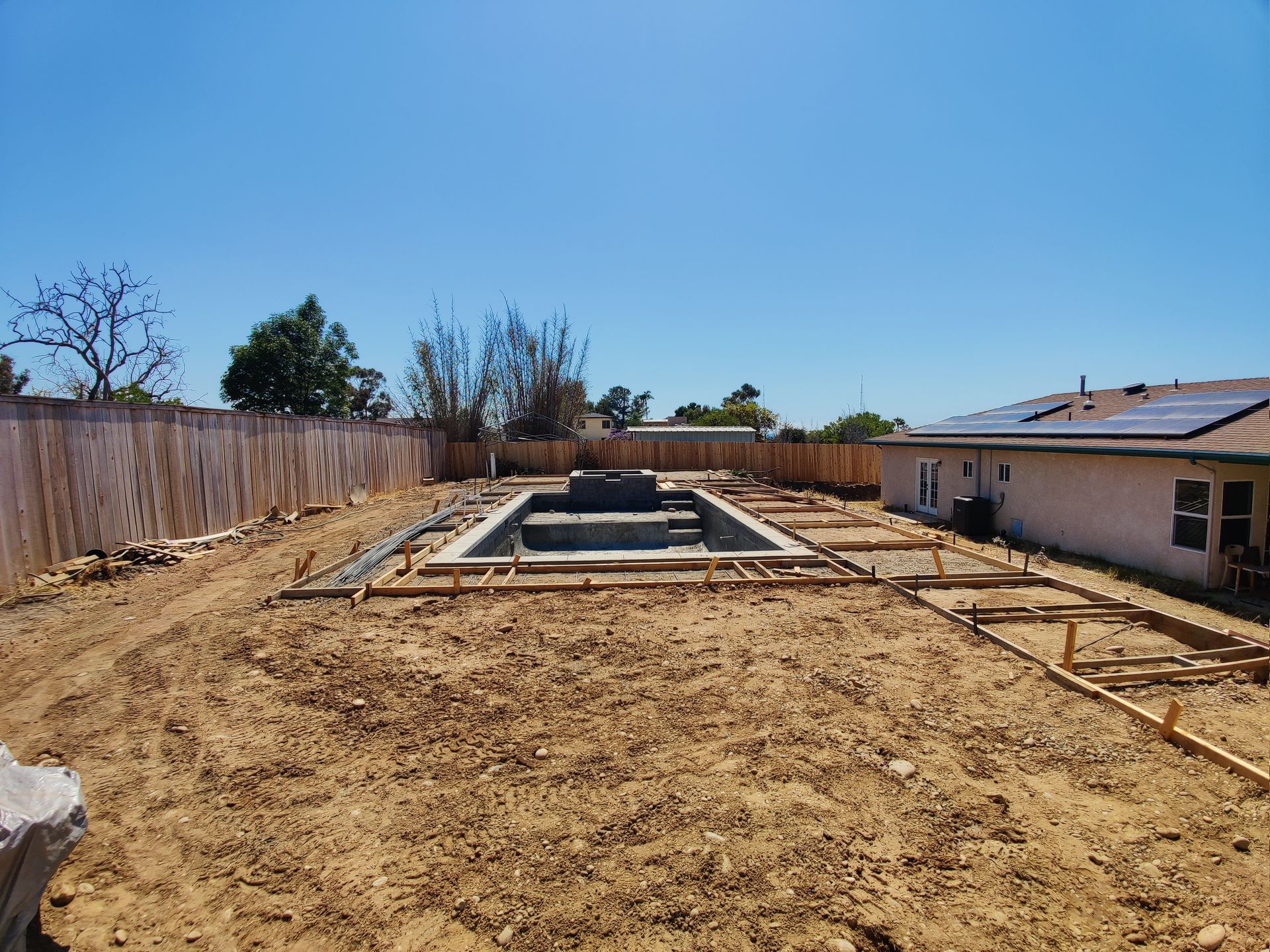 A swimming pool is being built in the backyard of a house.