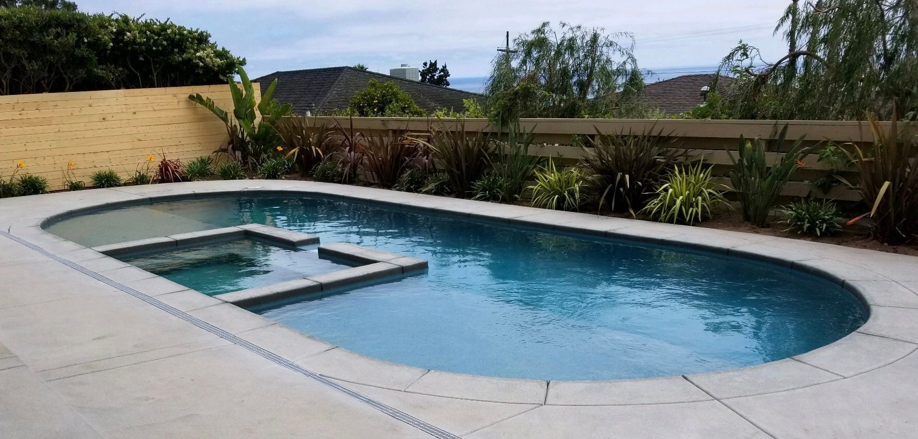 A large oval swimming pool with a hot tub in the backyard.