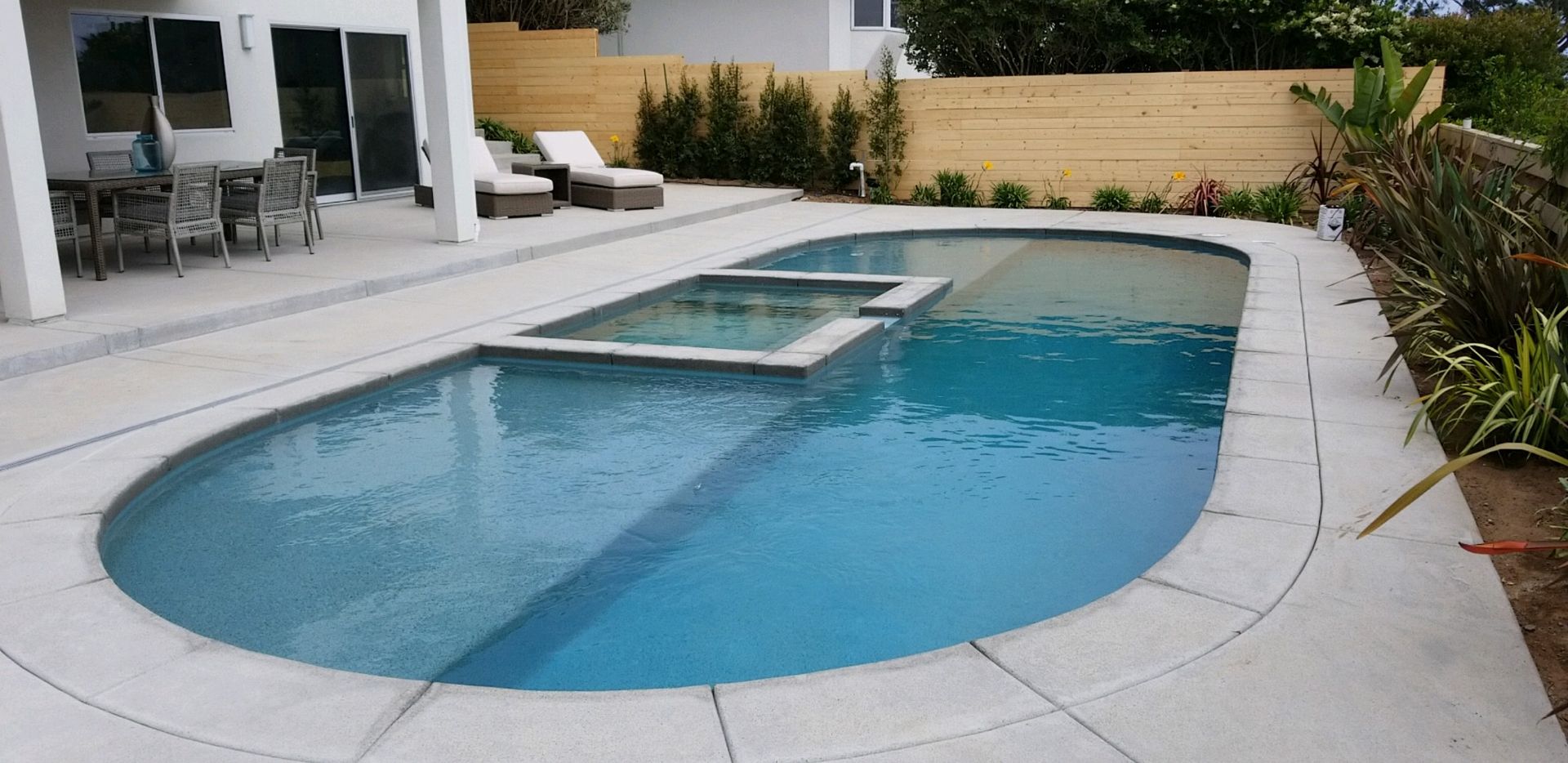 A large oval shaped swimming pool is in the backyard of a house.