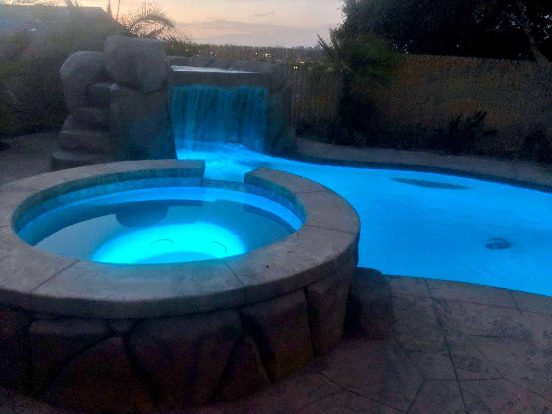 A swimming pool with a waterfall and a hot tub in the middle of it.
