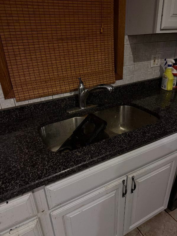A kitchen sink with a black granite counter top and white cabinets.
