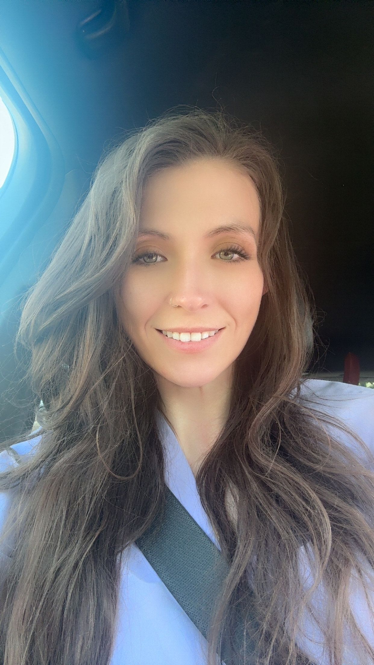 A woman with long hair is smiling while sitting in a car.