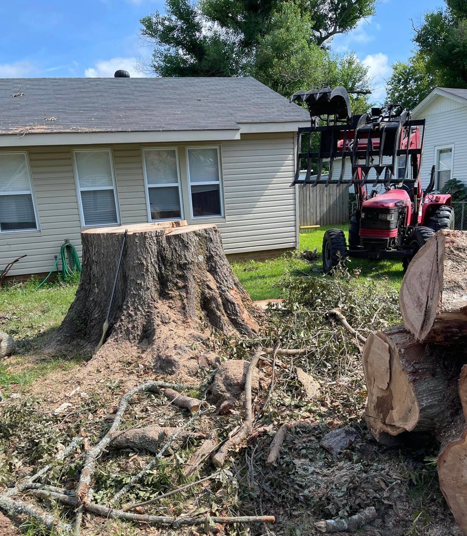 A tractor is cutting down a tree stump in front of a house.