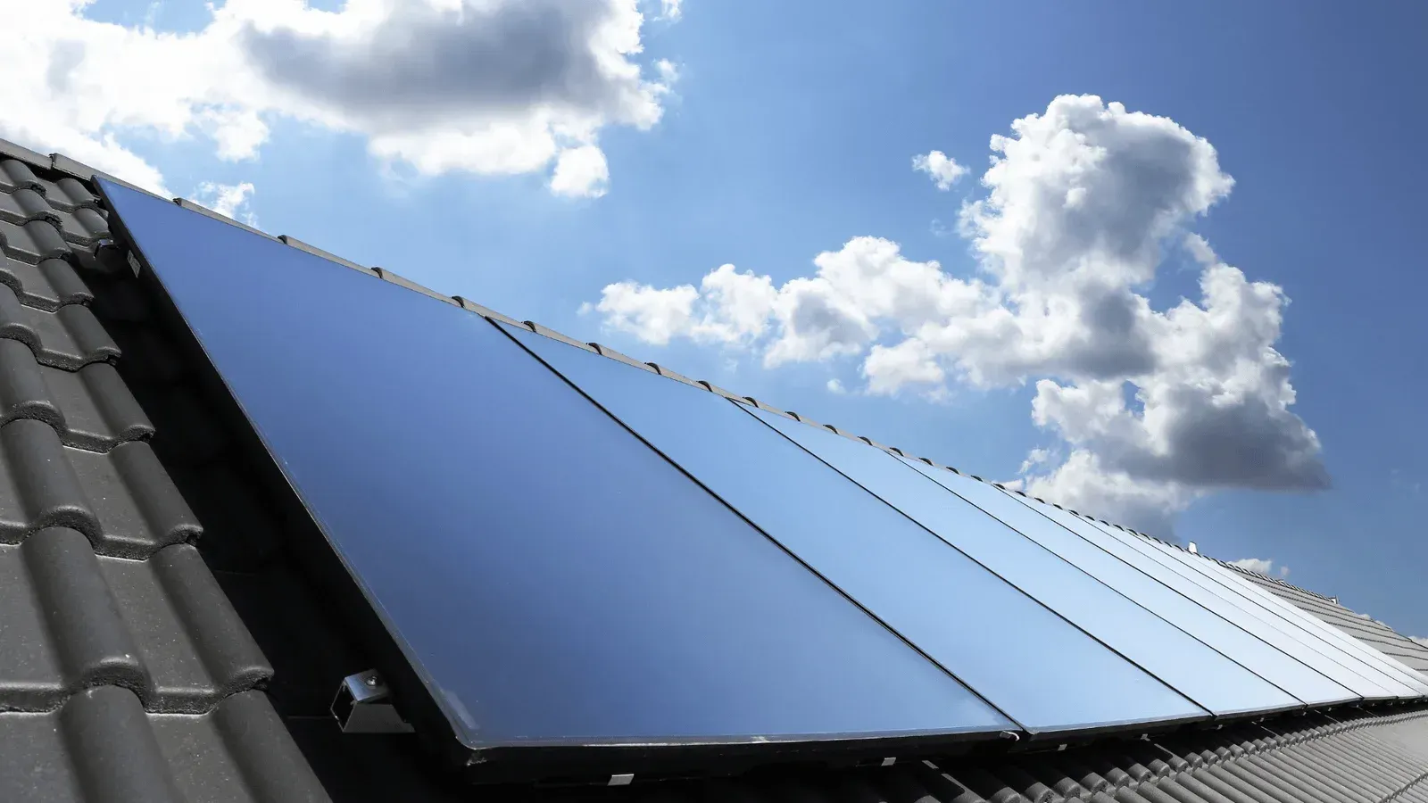 A row of solar panels on a roof with a blue sky in the background.