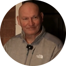 Bald man in gray jacket smiles; a small microphone hangs from his shirt.