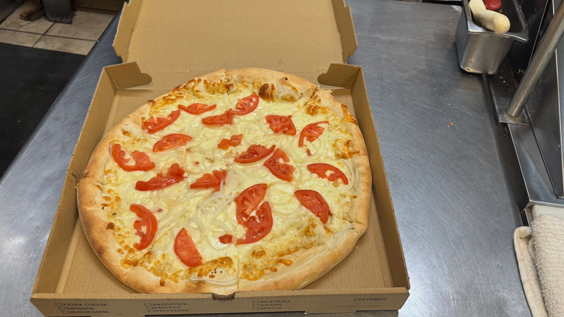 A pizza with tomatoes and cheese is in a cardboard box.