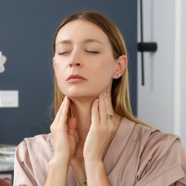 A woman with Hashimoto’s Thyroiditis is feeling both sides of her neck