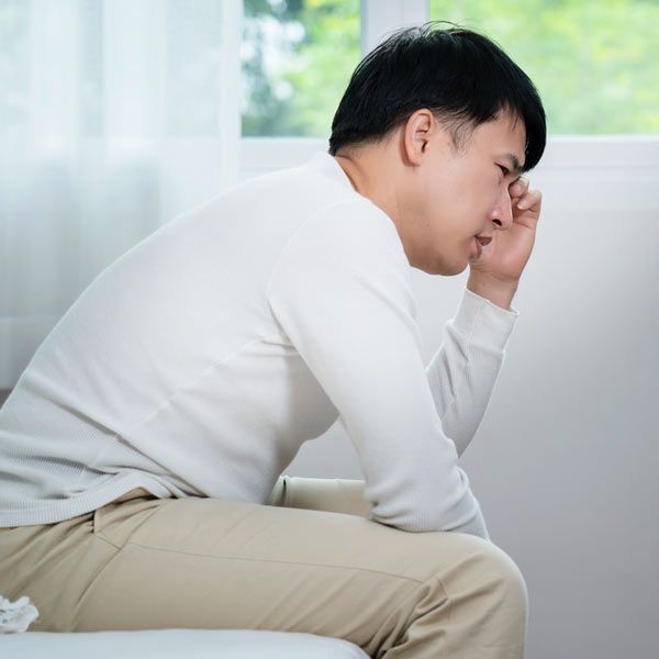An Asian man with Low Testosterone is sitting at the edge of the bed, tired and frustrated