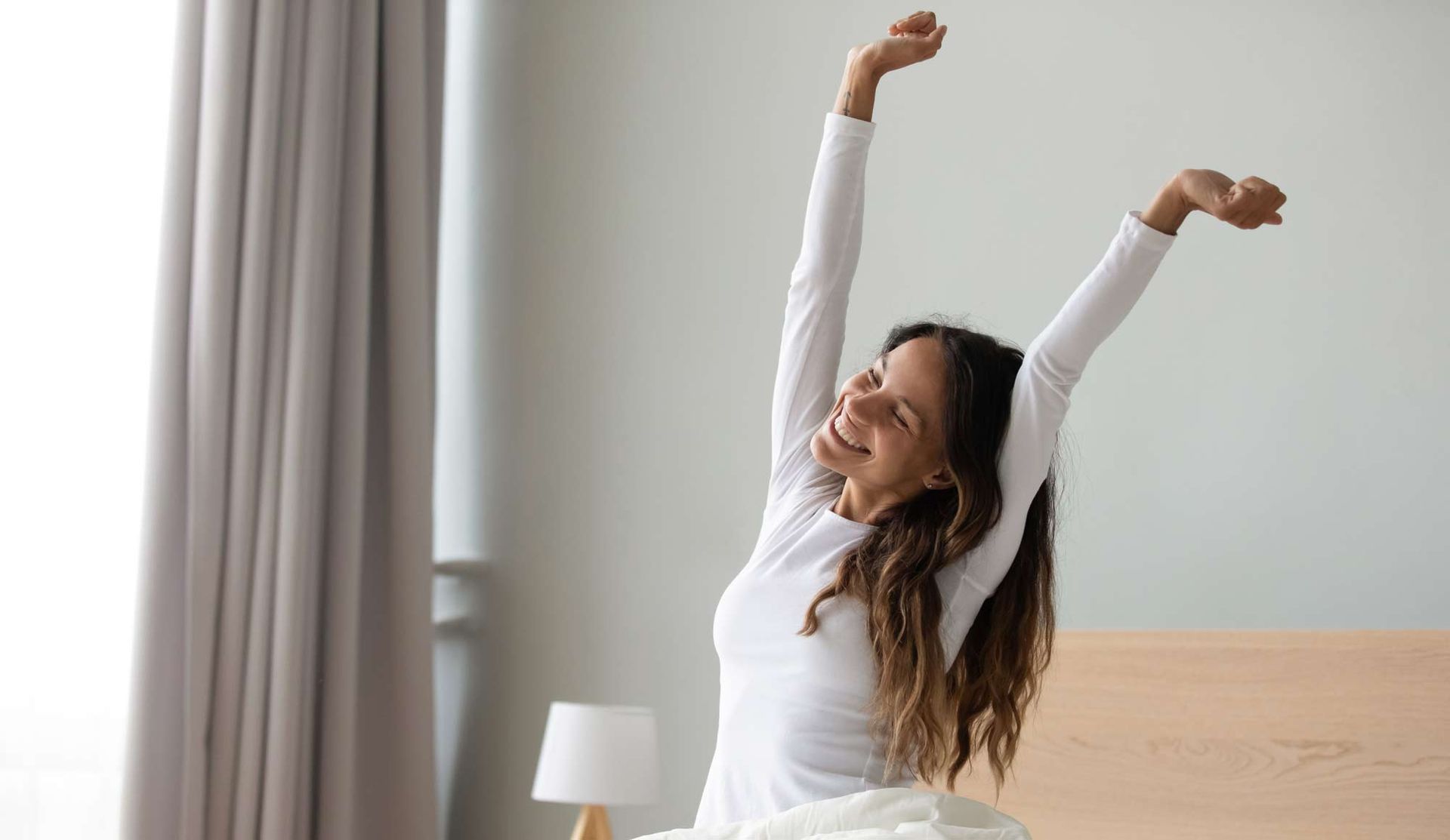 A woman is sitting on a bed with her arms outstretched. Better Energy By Better Eating
