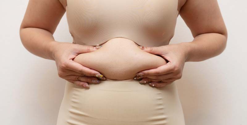 Woman in shapewear holding belly fat considering collagen for weight loss.