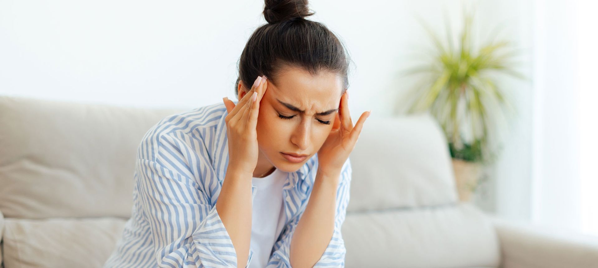 A woman is sitting on a couch with her head in her hands. Natural Headache Relief