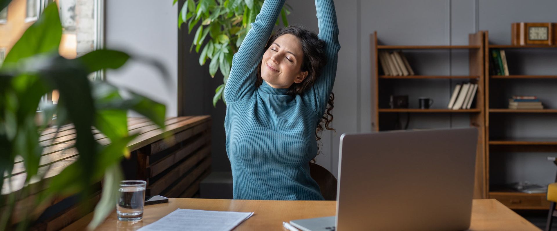 A woman is stretching her arms while sitting at a desk in front of a laptop computer. Introducing an