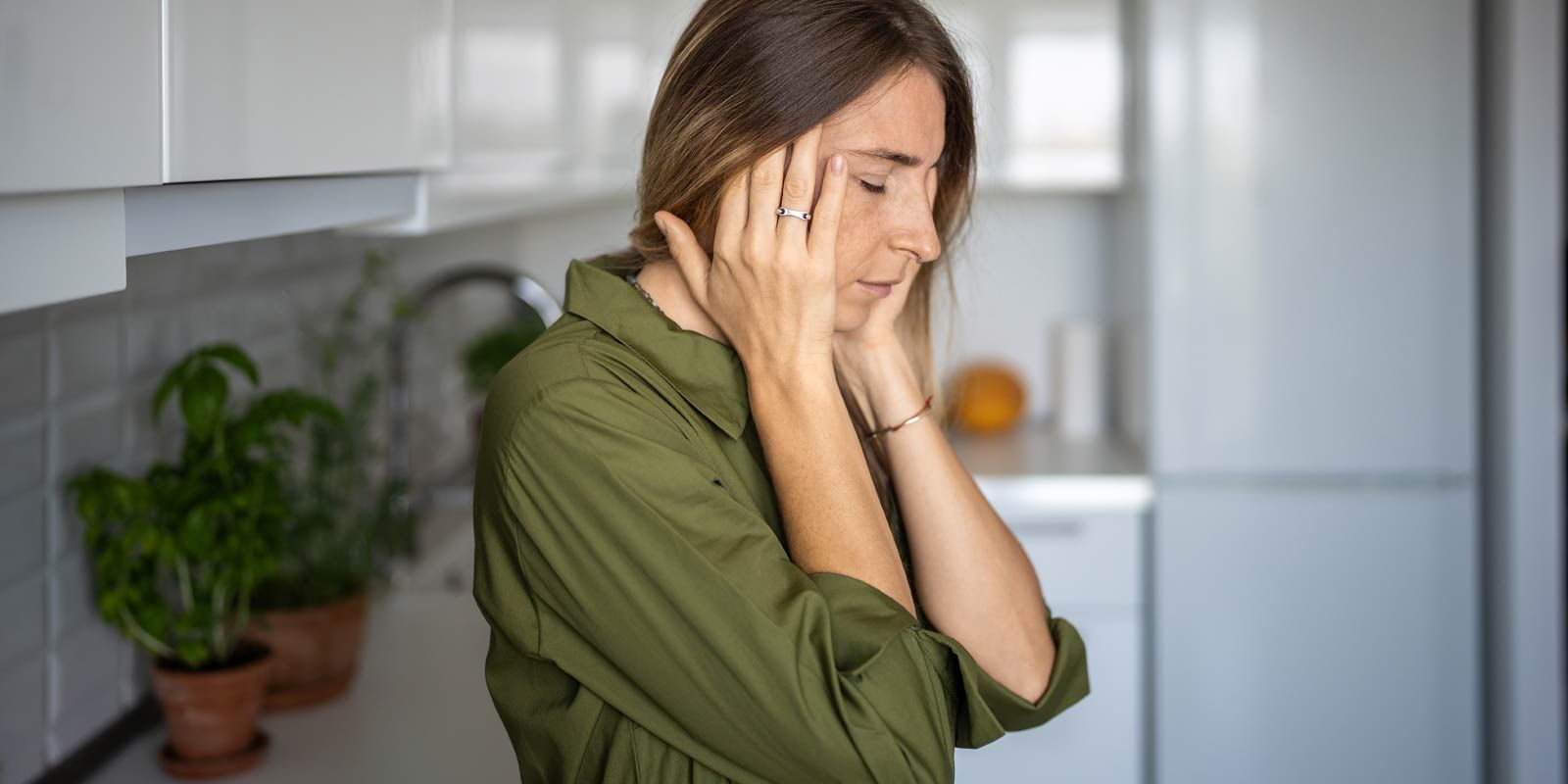 A woman is standing in a kitchen with her hands on her face, representing Premenstrual Dysphoric Disorder Remedies NYC by Dr. Alicia Armitstead.
