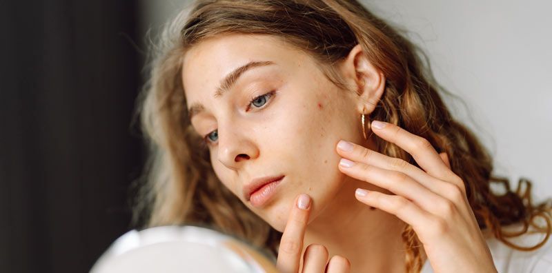 Woman looking in a mirror, touching her face, with a concerned expression. Skin Care from the Inside vs. the Outside
