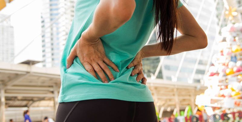 A woman in athletic wear is holding her lower back, experiencing the warning signs of sciatica