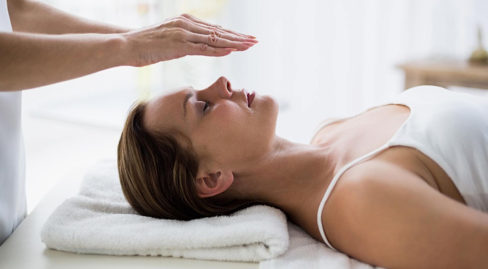 A woman is lying on a bed getting a Reiki healing treatment.