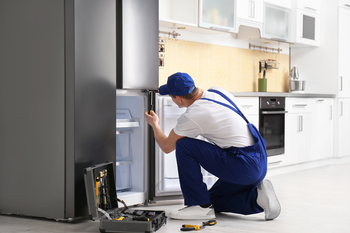 A man is repairing a refrigerator in a kitchen.