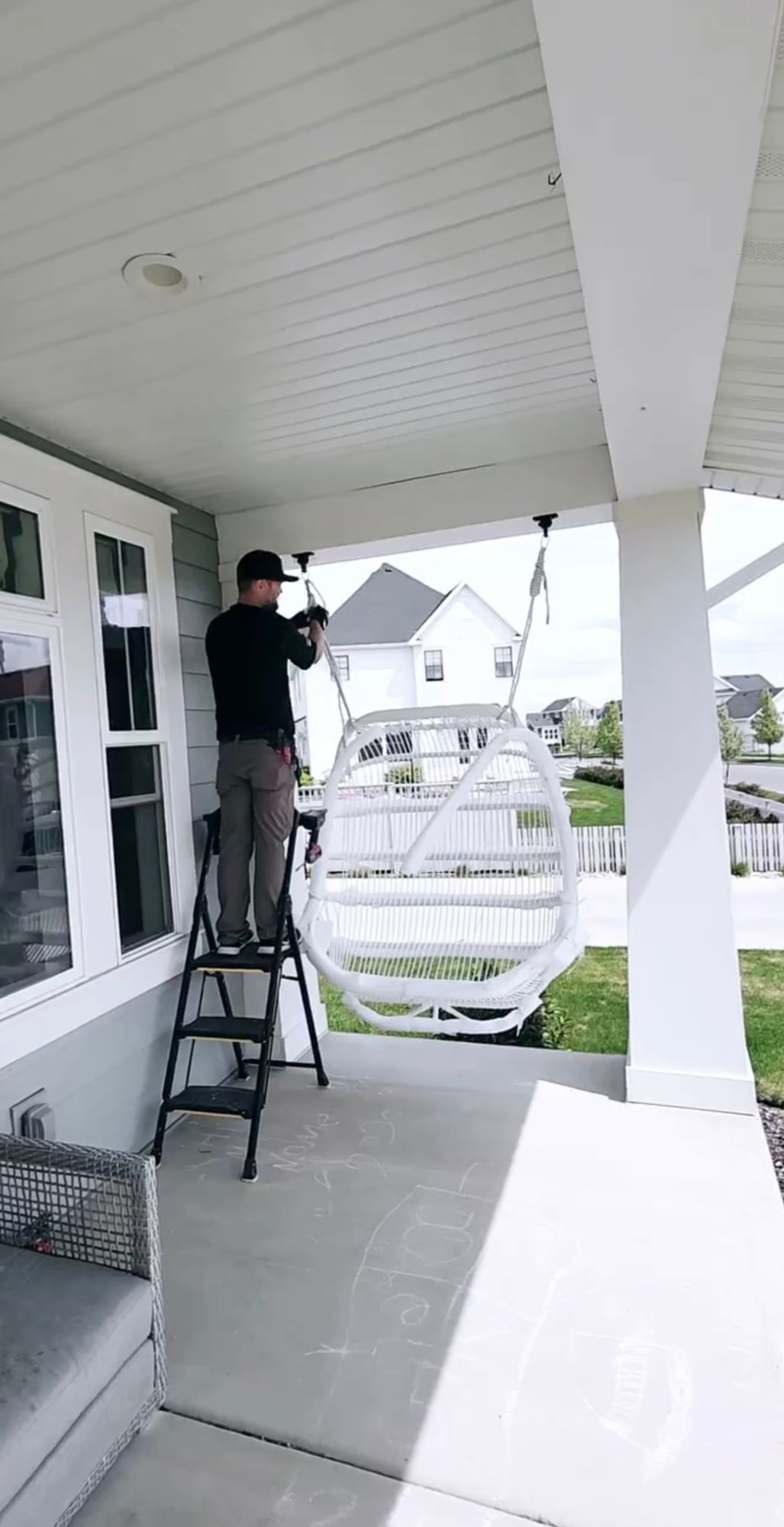 A man is standing on a ladder on the porch of a house.