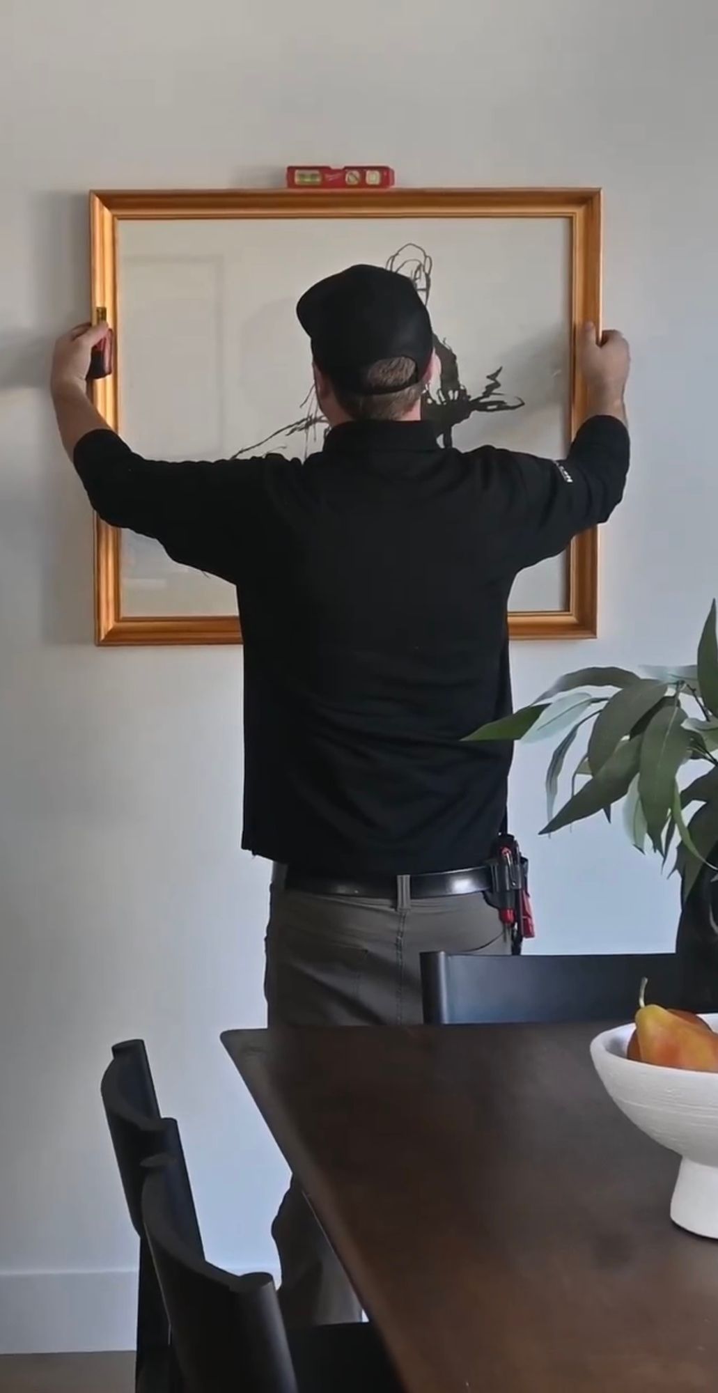 A man is hanging a picture on a wall in a dining room