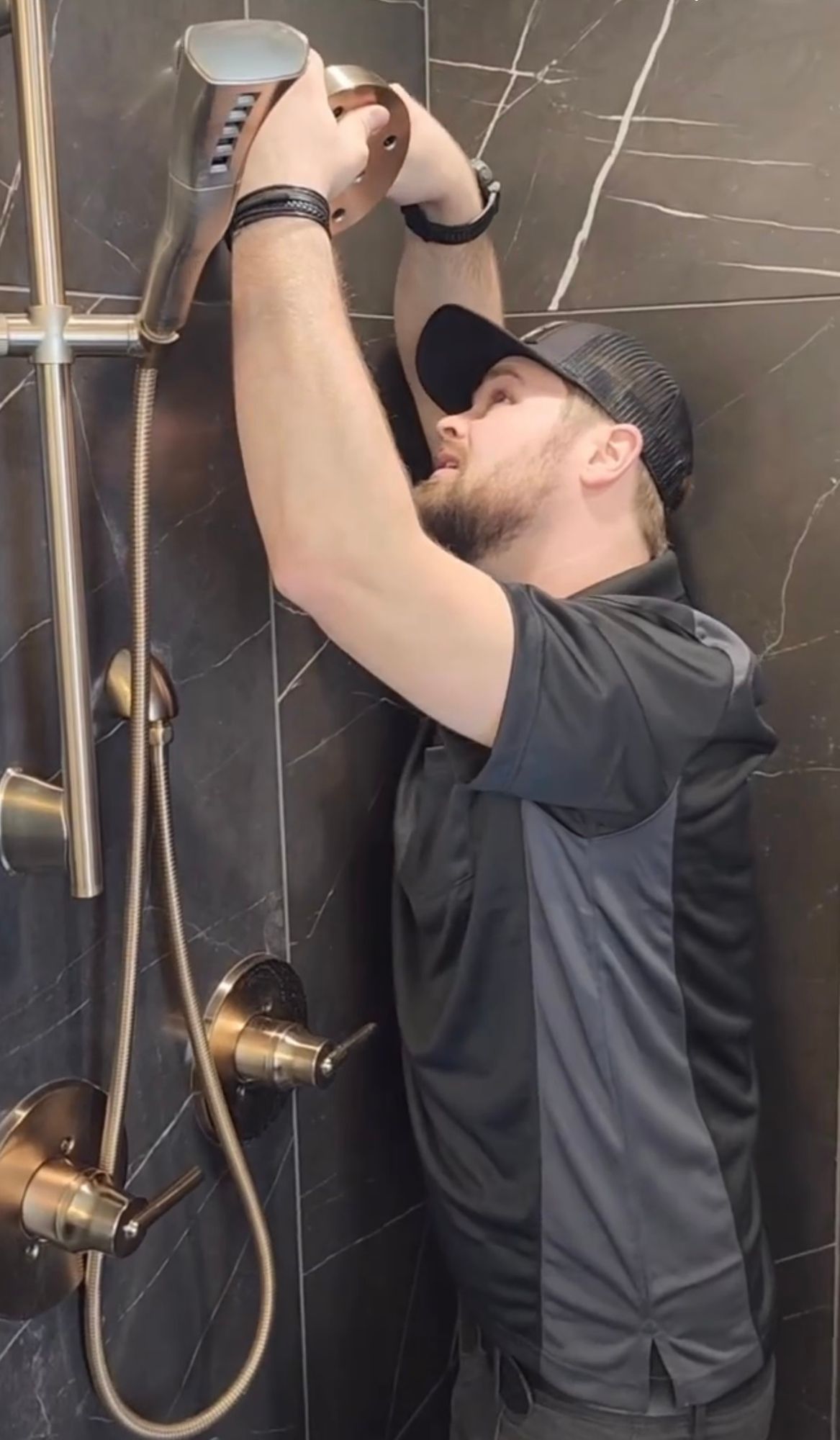 A man is fixing a shower head in a bathroom.