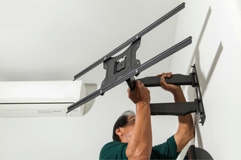 A man is installing a flat screen tv mount on a wall.
