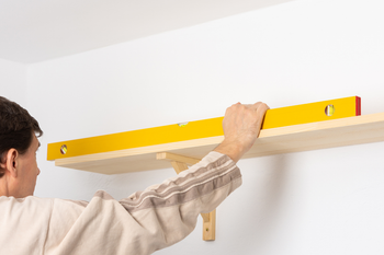 A man is measuring a wooden shelf with a level.