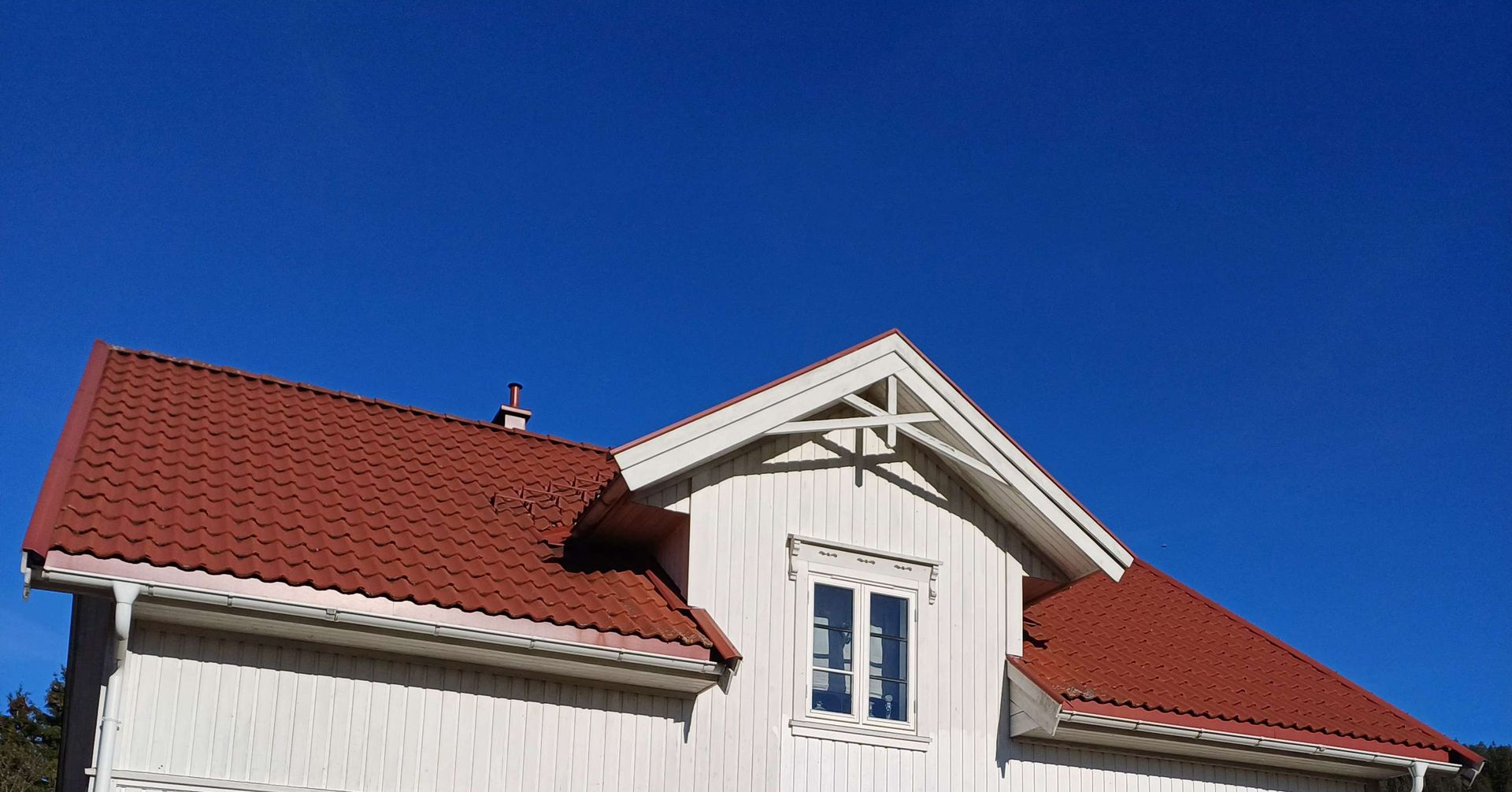 Det røde takshinglet og den hvite fasaden til et hus under en klar, dypblå himmel.