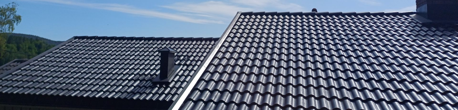 A roof with brown tiles and a chimney, next to a grassy hill and dirt path.