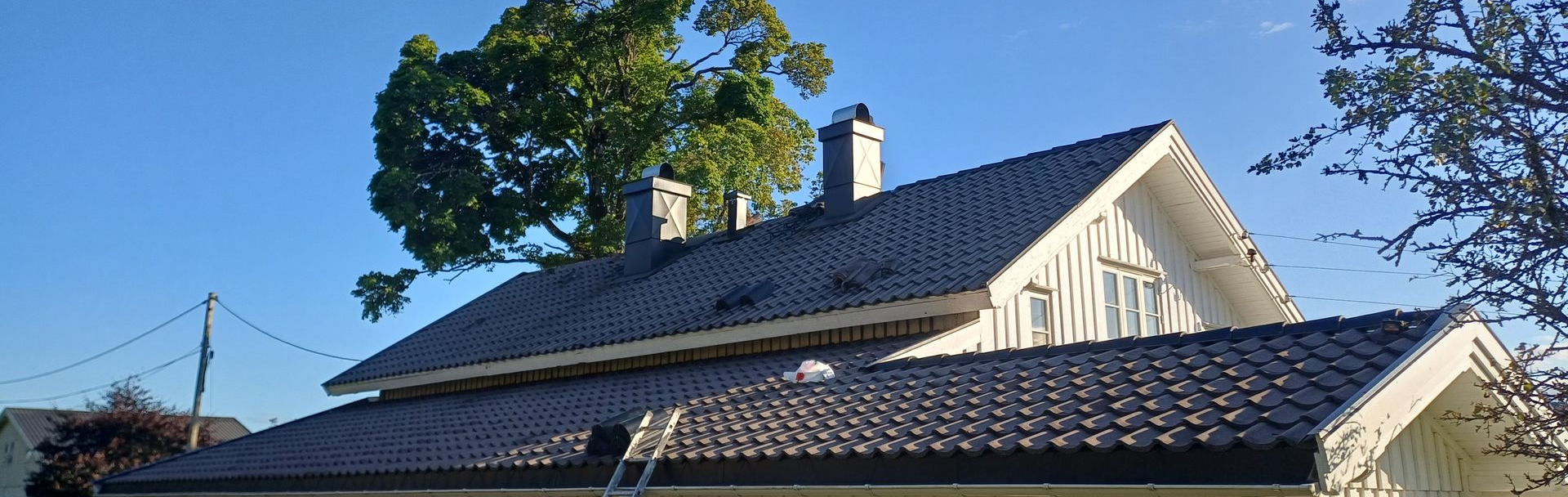 Brown tiled roof, top-down view; residential area with green foliage and asphalt road in the background.
