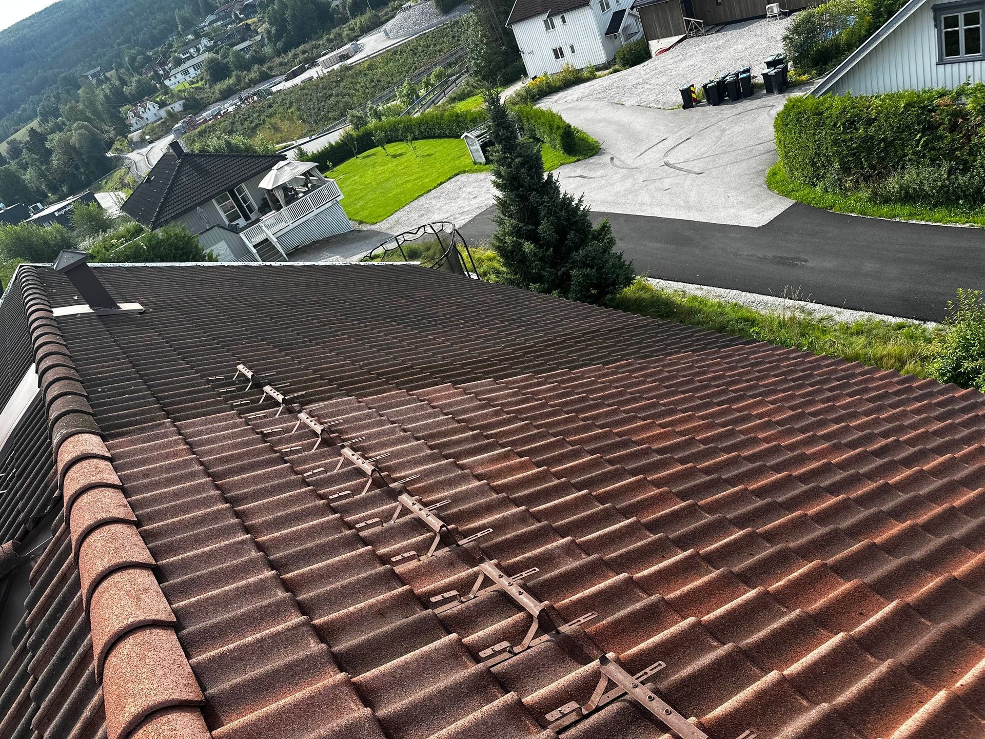 Brown tiled roof with metal strips, angled view with houses and greenery in the background.