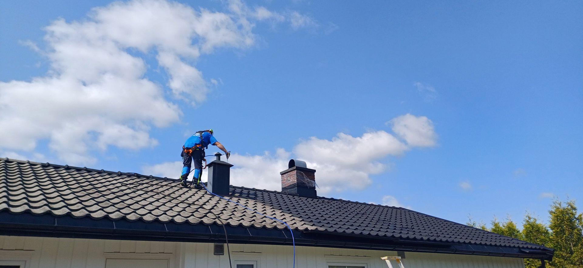 A person working on the roof of a house, cleaning a chimney, with a blue sky background.