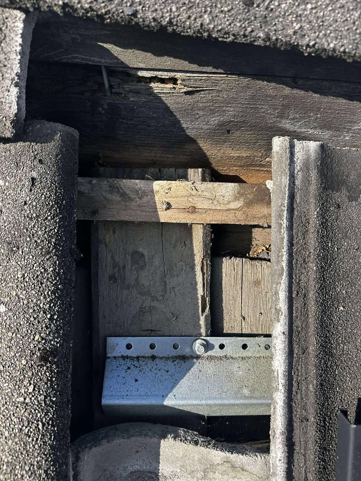 Close-up of a roof tile and wooden framework. A metal bracket is visible beneath the framework.