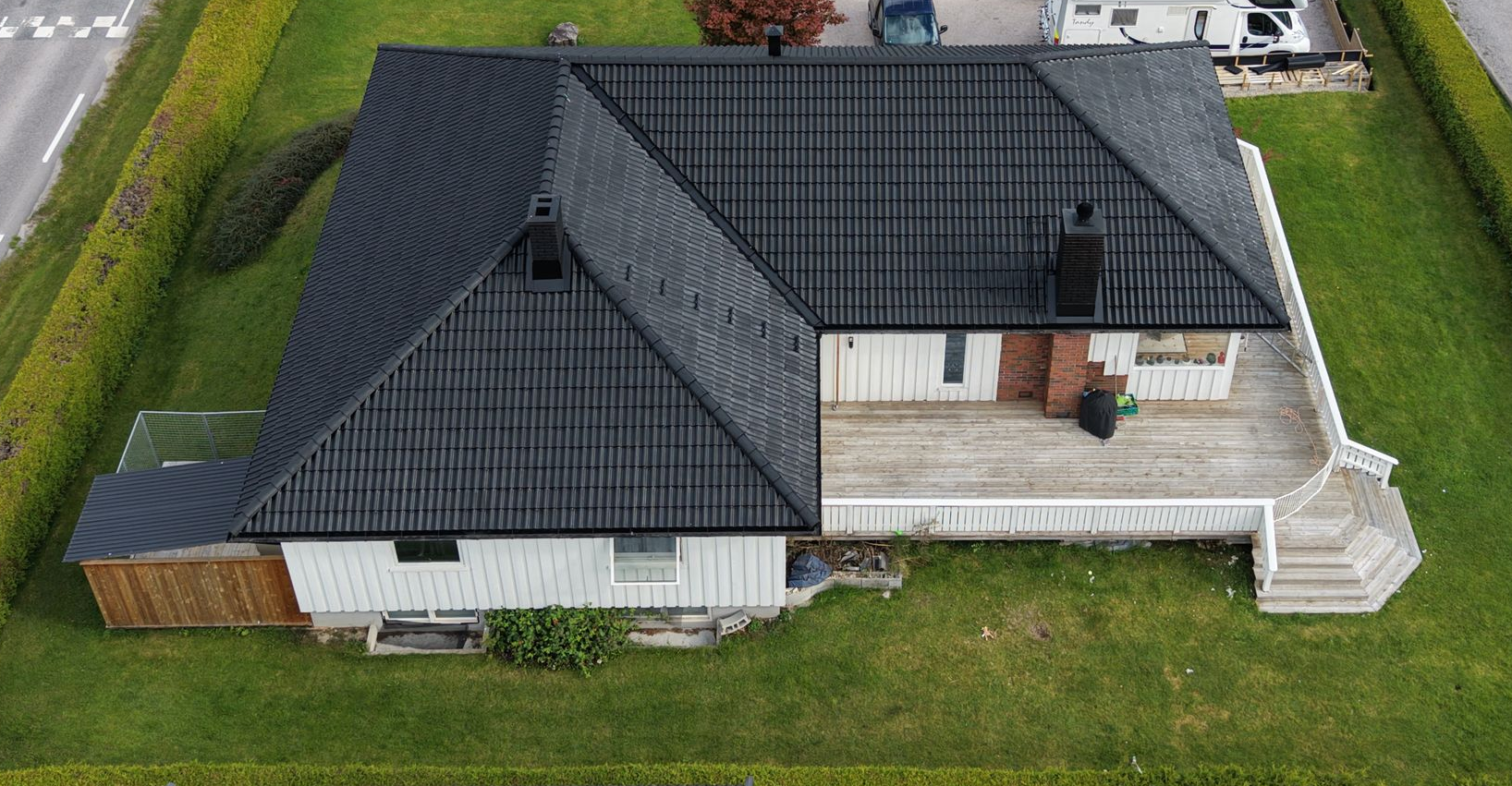 A roof with brown tiles and a chimney, next to a grassy hill and dirt path.