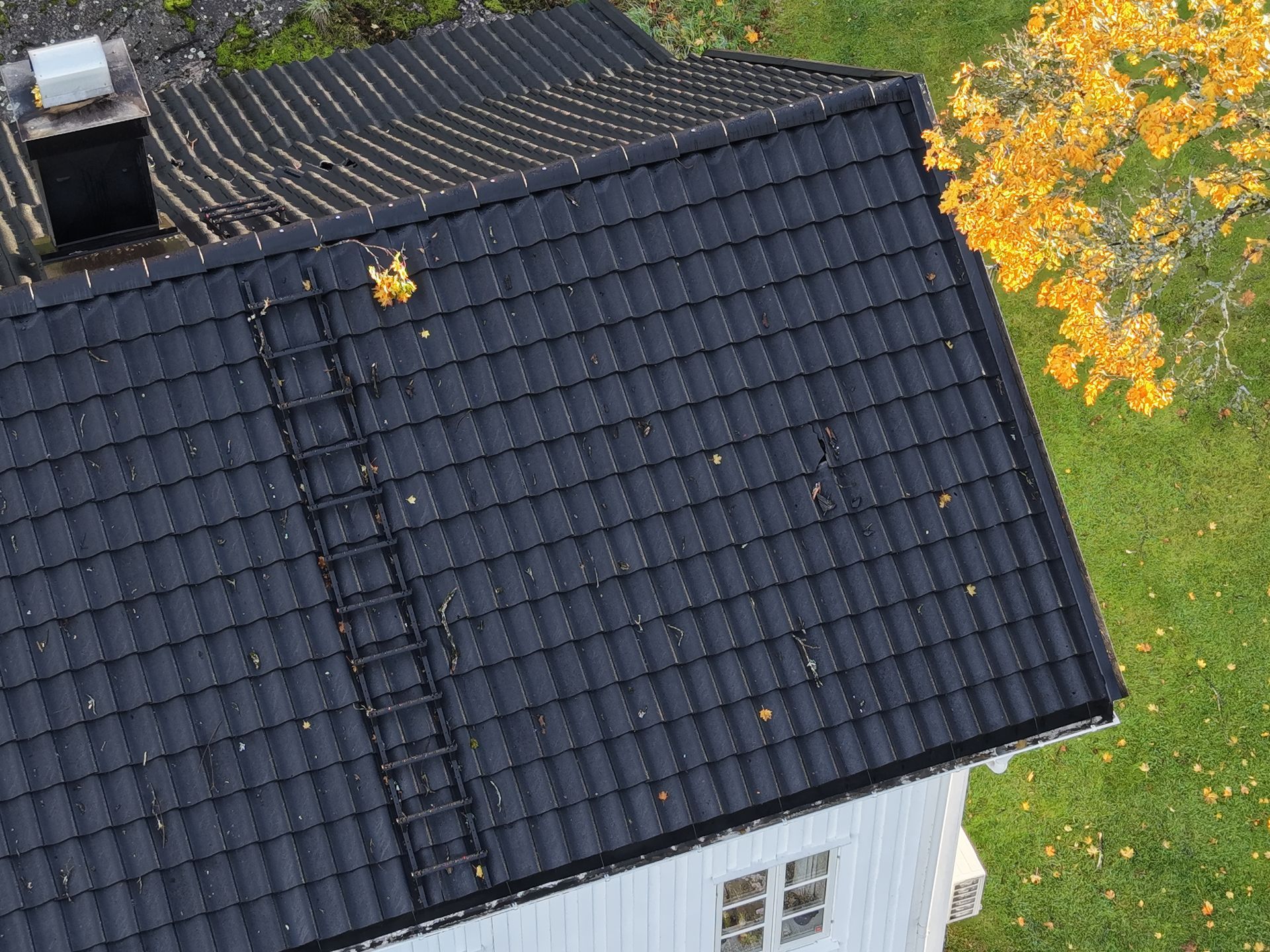 A roof with brown tiles and a chimney, next to a grassy hill and dirt path.