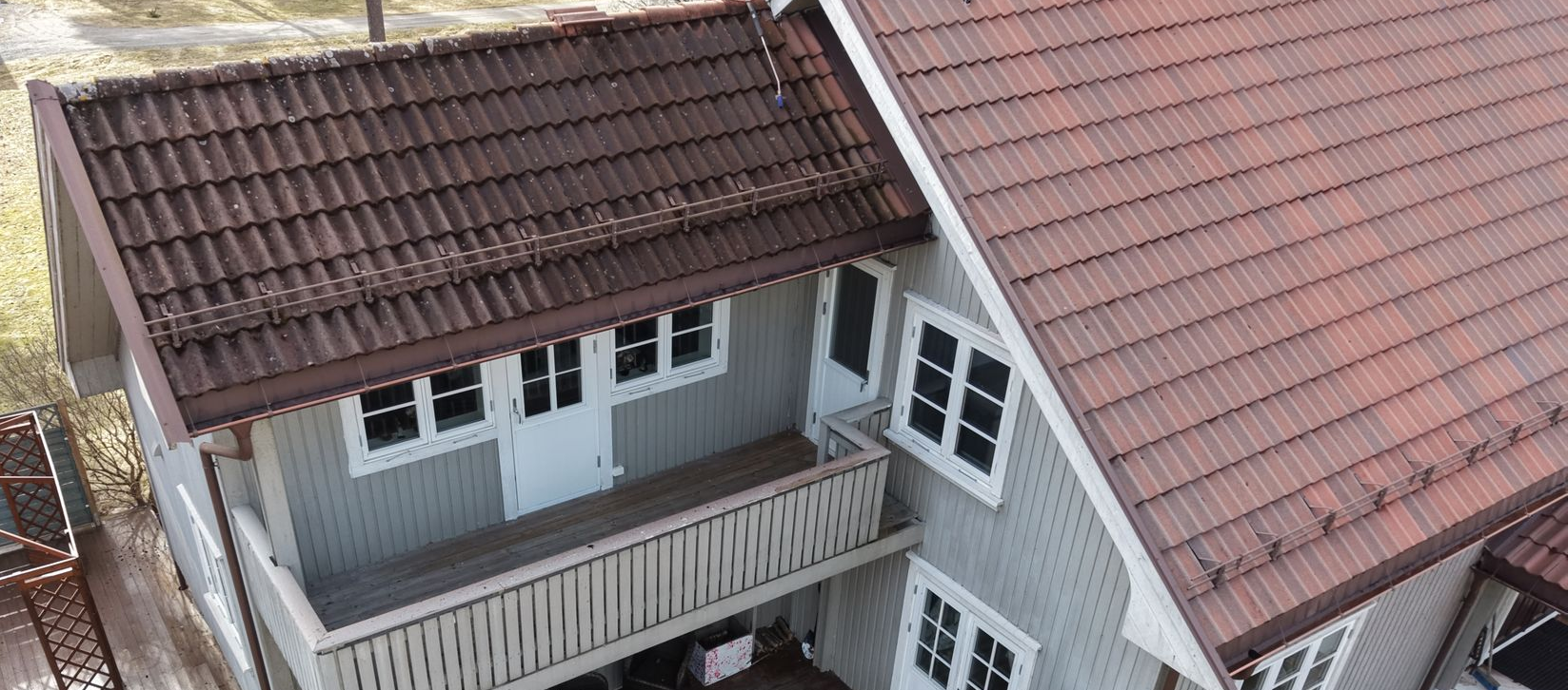 Høyvinkelutsikt av et grått trehus med rødt tegltak, balkong og hvite vinduer.