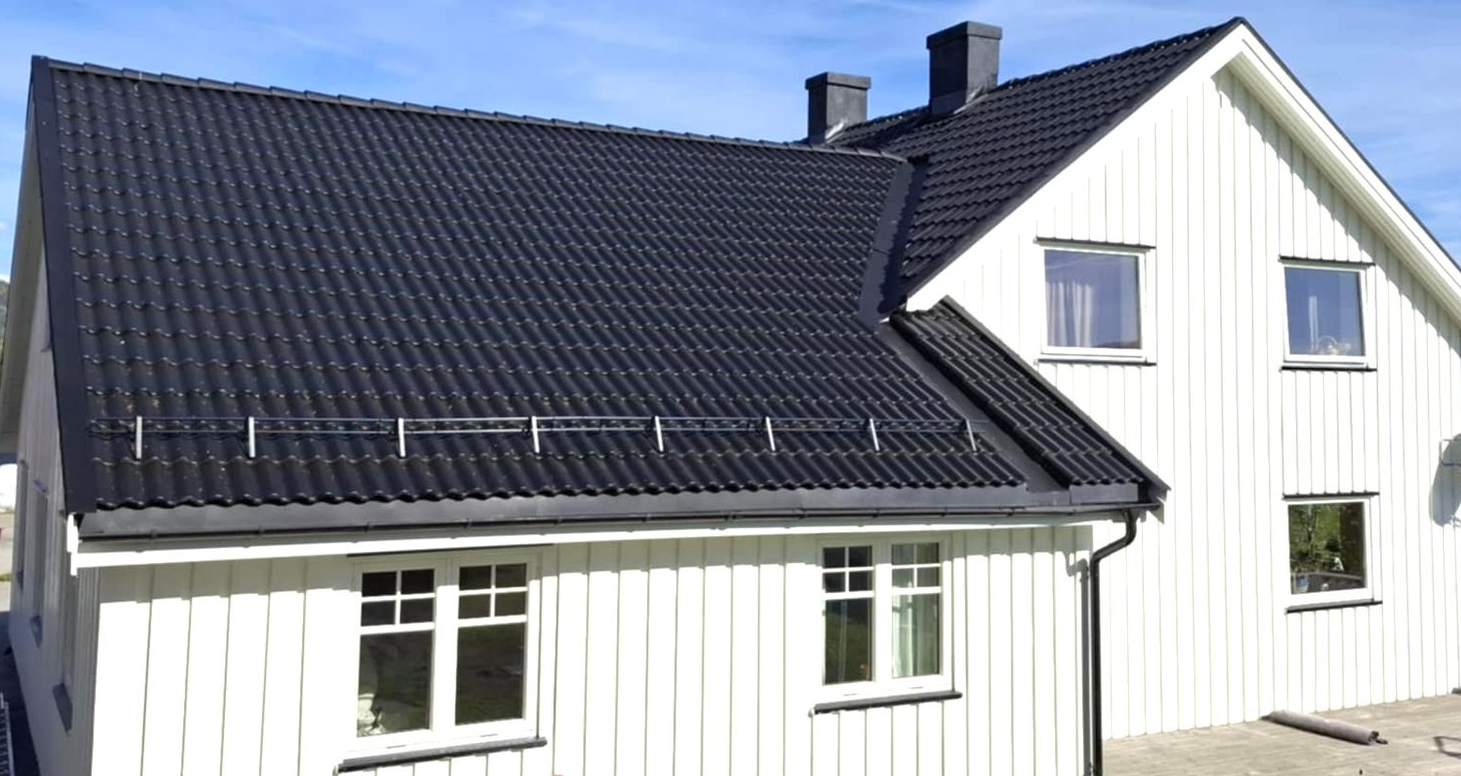 A close-up view of a dark gray tiled roof with a chimney and a person with safety gear.