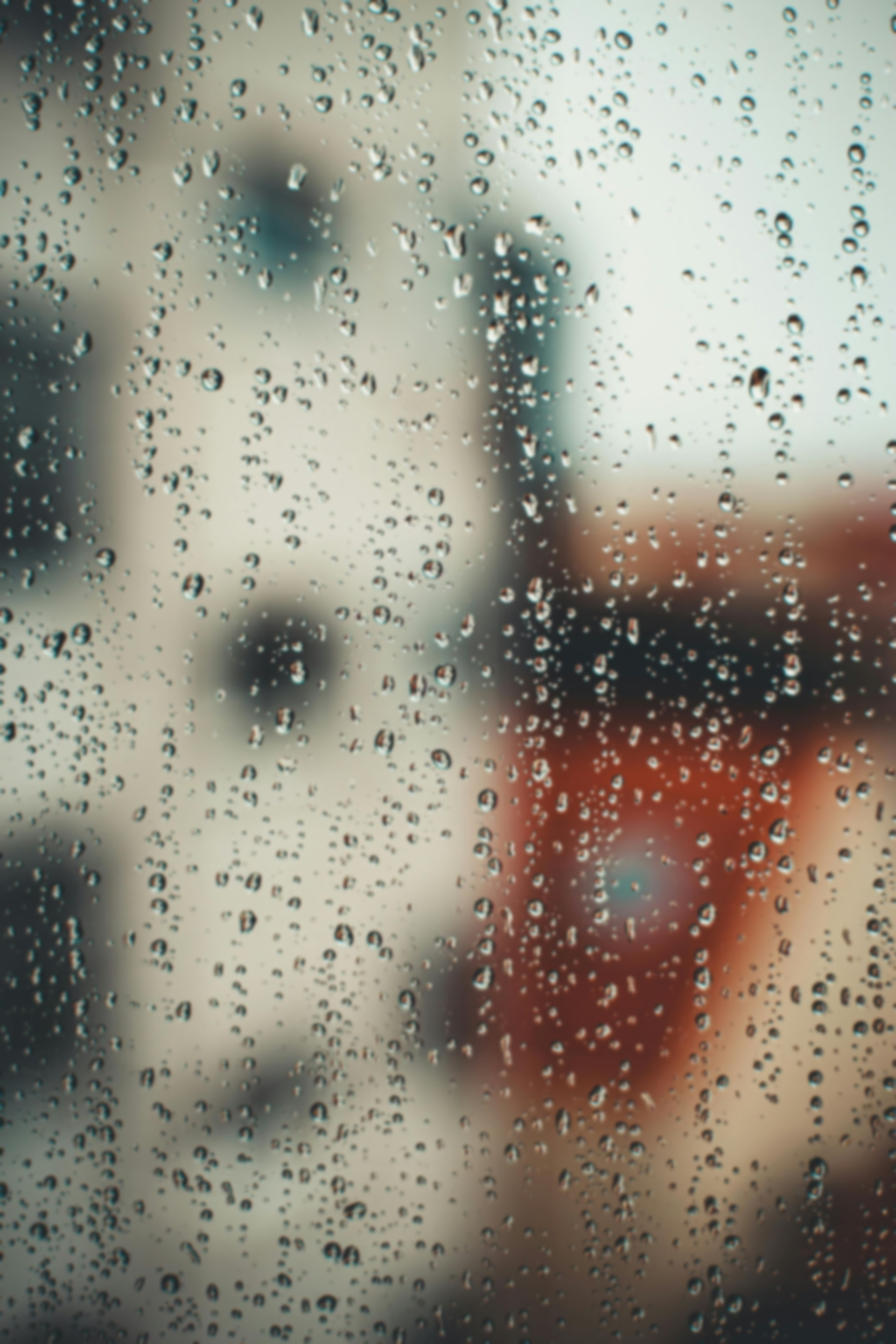 Raindrops on a window pane with a blurred urban building background in soft, muted tones.