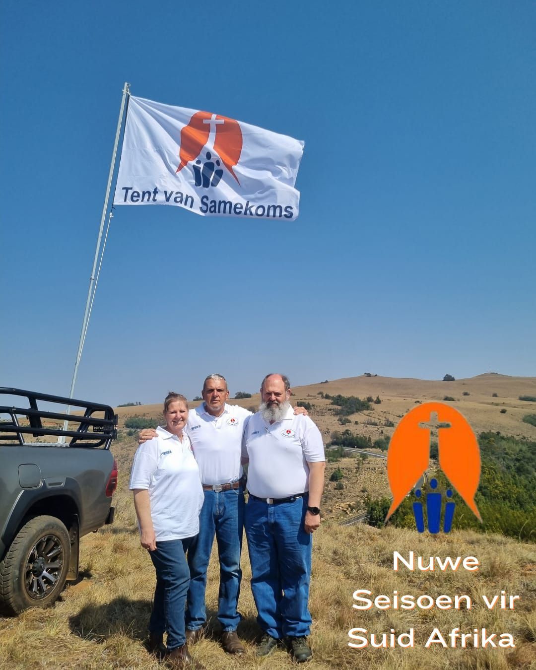 A group of people standing in front of a truck with a flag in the background.