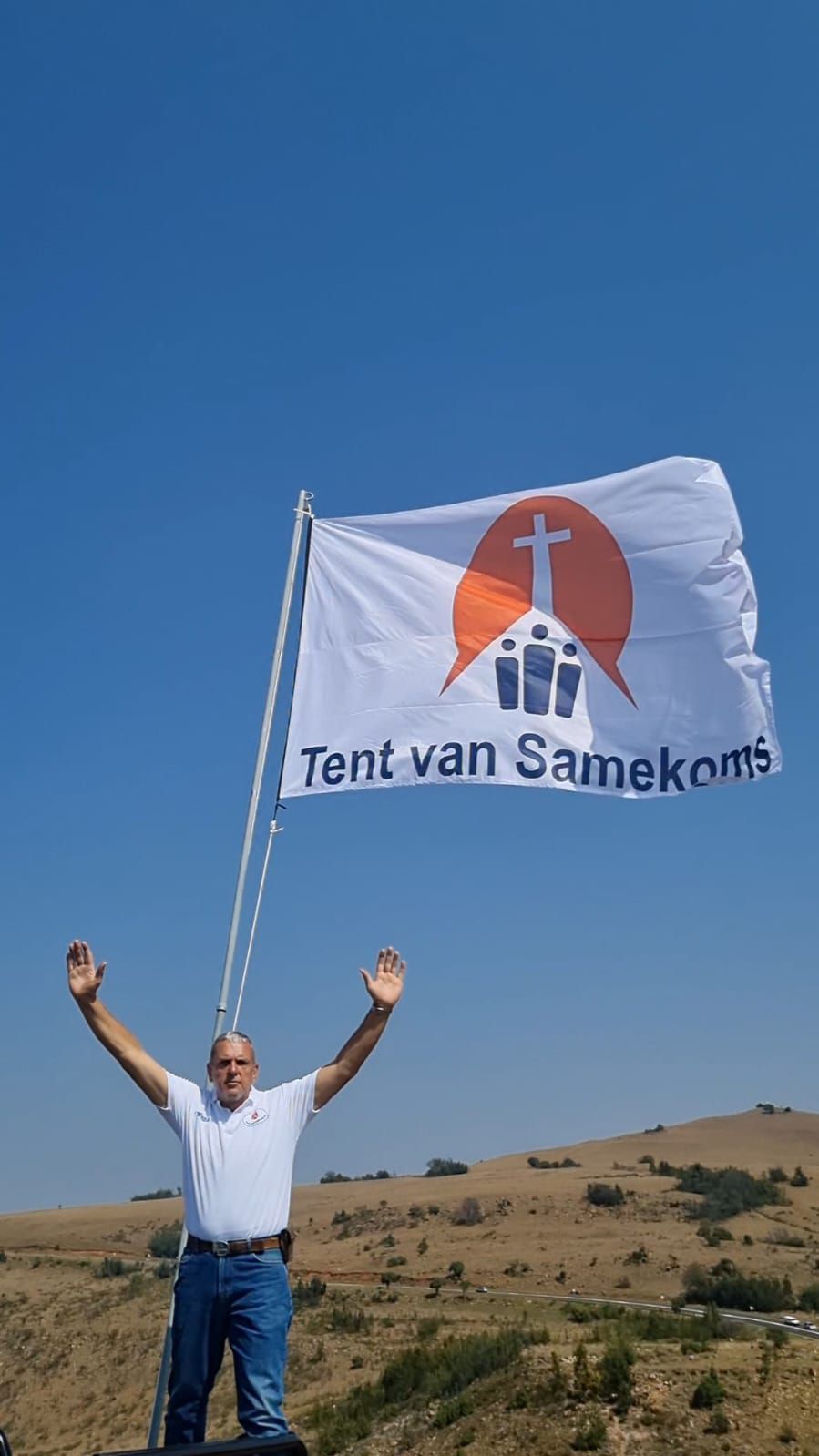 A man is standing on top of a hill holding a tent van samekoms flag.