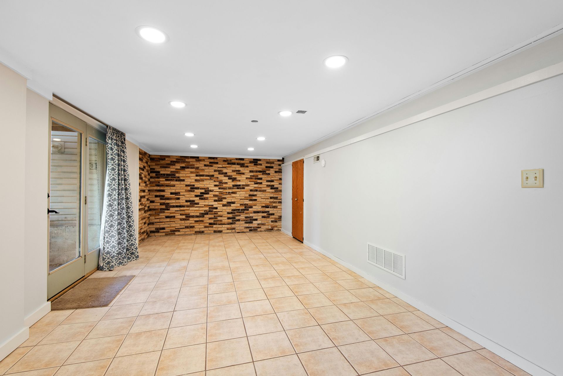Empty room with wood wall, French doors, white walls, and light-colored tiled floor.