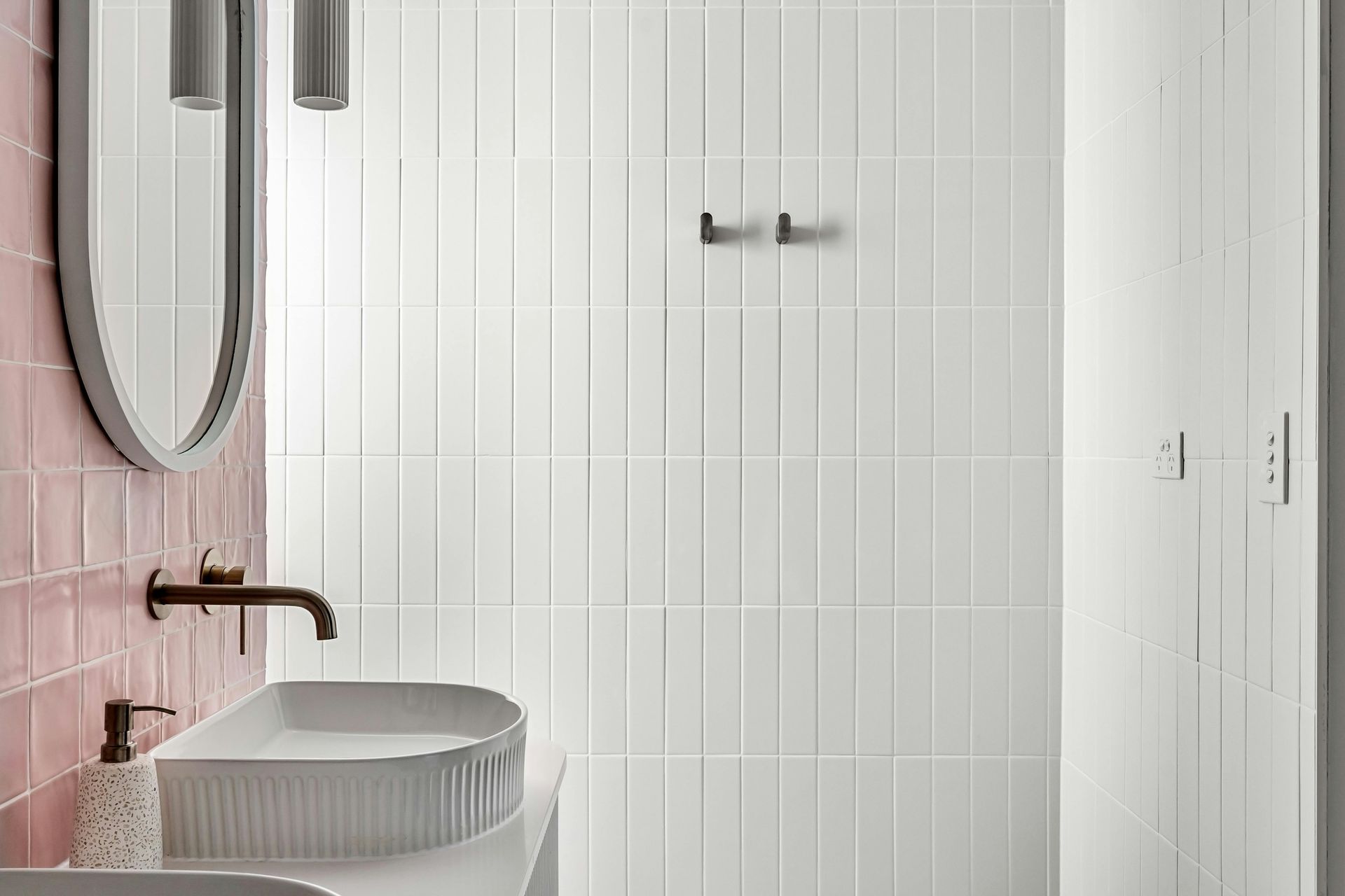 Modern bathroom with pink tile, white elongated wall tile, and a curved mirror above a white sink.