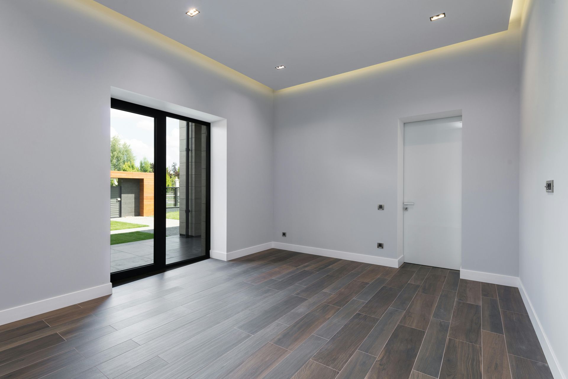 Empty room with dark wood floor, light gray walls, glass door, and white door.