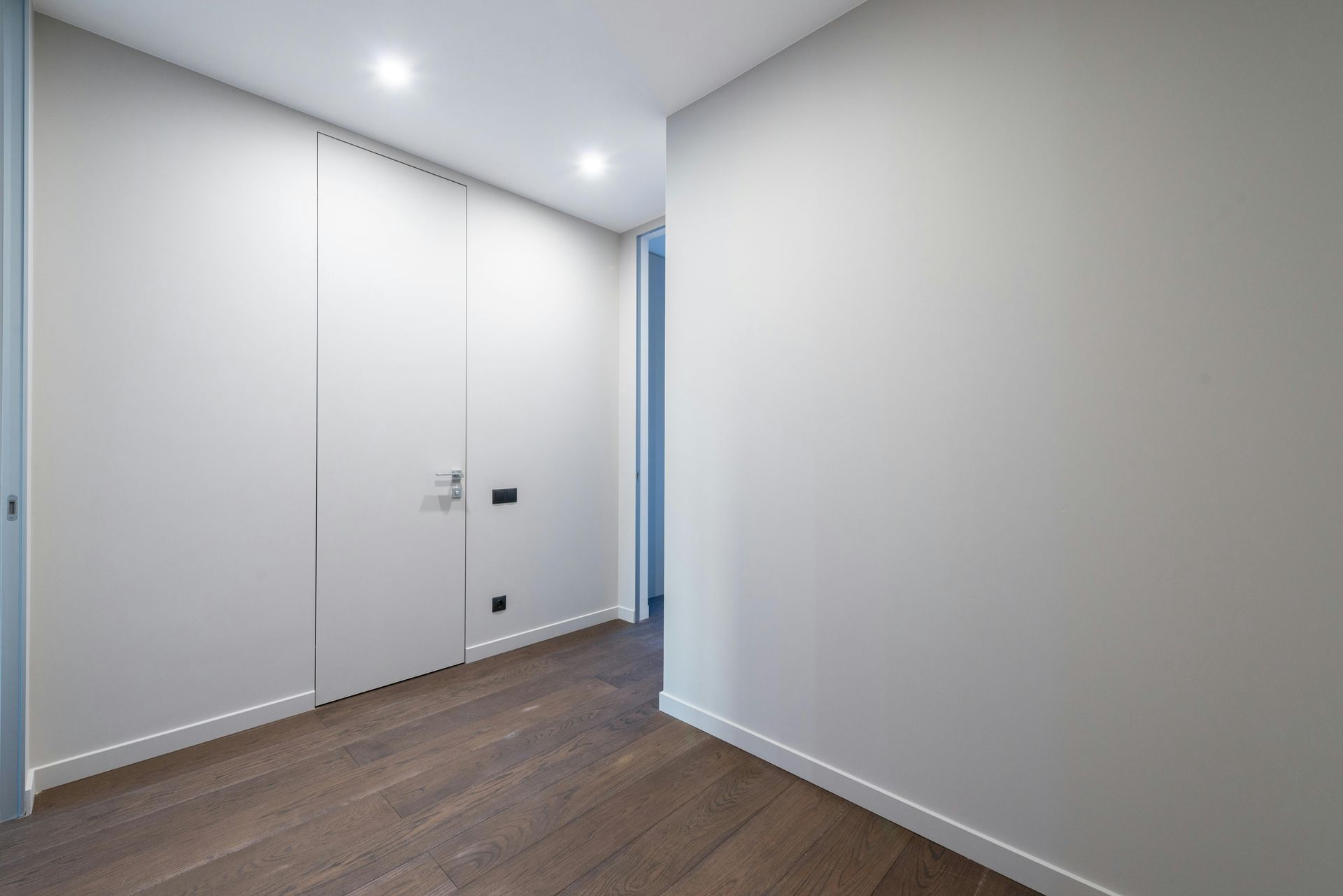 Empty hallway with white walls, closet doors, and hardwood floors.