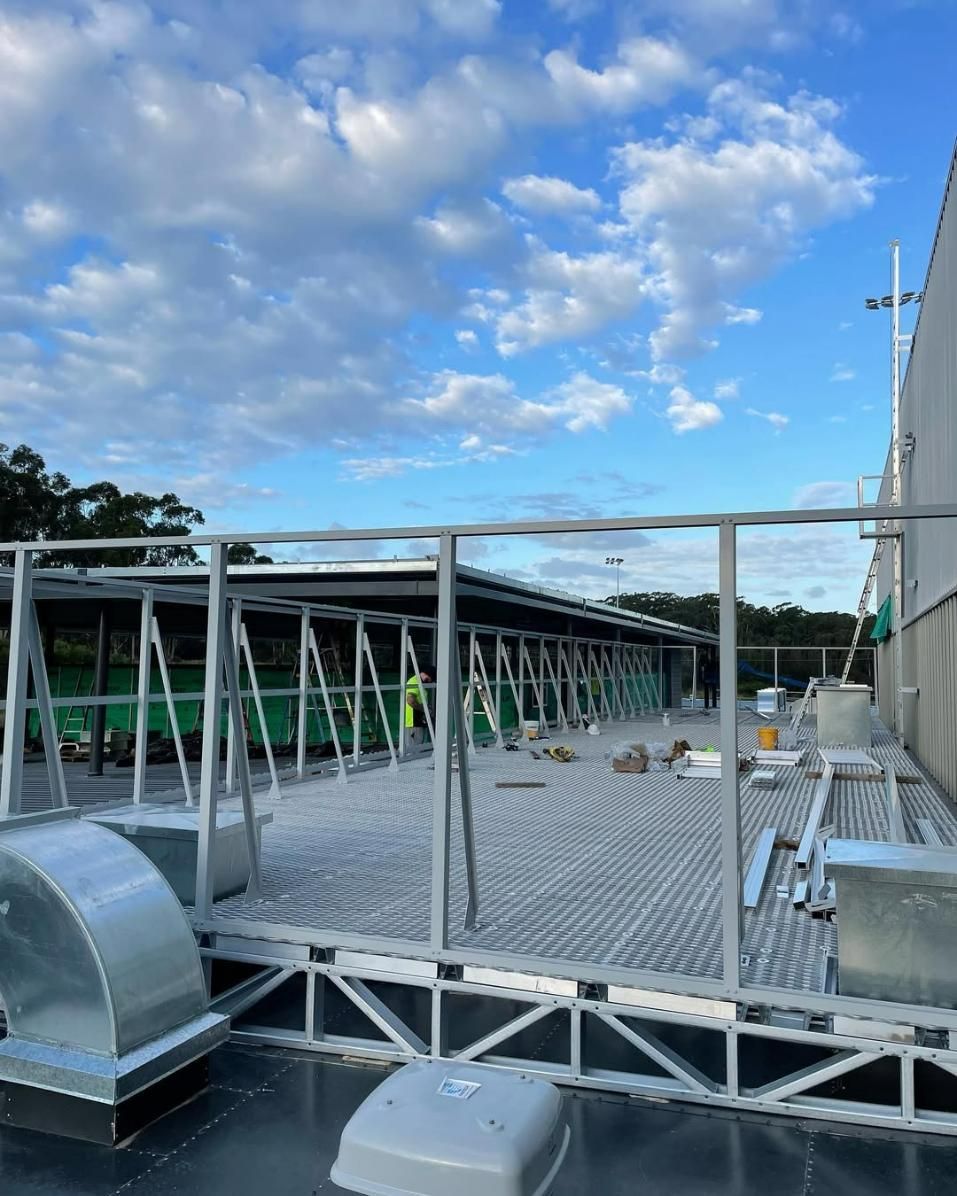 A Large Metal Structure Is Being Built on The Roof of A Building — Site Safety NSW in Central Coast, NSW